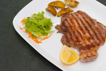 Grilled meat steak with lemon, carrots, lettuce and potatoes. Juicy and very tasty dish of Italian cuisine