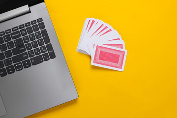 Playing Cards and laptop keyboard on yellow background. Online poker casino. Top view
