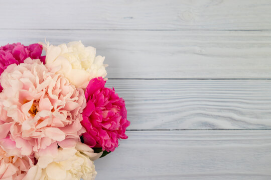 white and pink peonies in a vase against a wood background