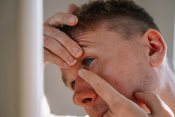 Obraz premium The young blond man puts on contact lenses