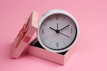 Clock in a gift box on a pink background.