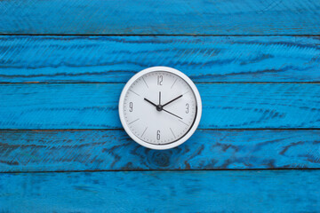 White clock on blue wooden background. Time running away. Top view