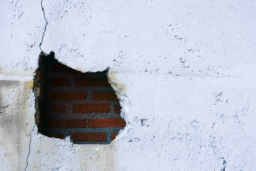 Hole in broken wall and old bricks on white background. Large crack on the wall of an old brick house, crumbling plaster and broken, cracked bricks.