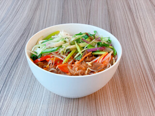 Vietnamese beef noodle bowl (Khom Duoi Bo) with fresh cucumber & sliced vegetables. Top view plate with traditional asian food with chopsticks on wooden table. Delicious authentic food in Vietnam.