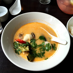 Traditional Thai soup Tom yum with seafood in a white bowl with a spoon on a black wooden background. Delicious authentic healthy Asian food for food hall decoration, poster, banner, menu.