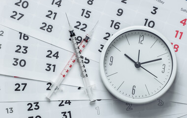 Two Syringe and clock on a monthly calendar close-up. Vaccination