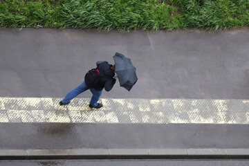 Rain in a city, man with umbrella running on wet sidewalk, top view. Rainy weather at summer, heavy windrun, 