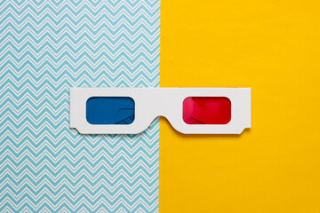 Retro 80s paper stereo 3D glasses with red-blue eye filters on a blue-yellow background. Top view