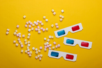 Anaglyph disposable paper 3d glasses with marshmallows on a yellow background. Top view. Pop art, minimalism