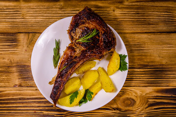 Plate with roasted ribeye steak on wooden table. Top view