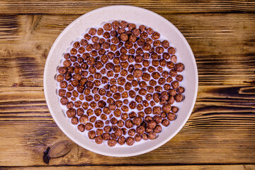 Ceramic plate with chocolate cereal balls in milk on wooden table. Top view