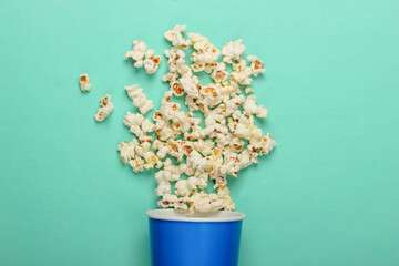 Movie time. Cardboard bucket of popcorn on mint green background. Top view
