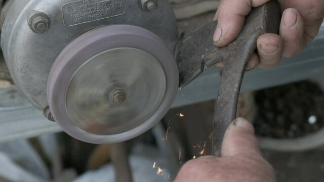 Close up view of senior man hands sharpening axe on lathe machine in slow motion