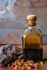 Still life with a square bottle of grape vinegar, raisins and ocher stone on a copper surface and...