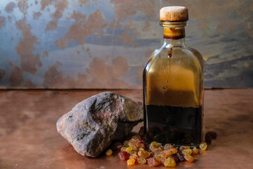 Still life with a square bottle of grape vinegar, raisins and ocher stone on a copper surface and rusty metal background. Copy space.