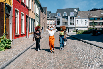 multiethnic girlfriends walking in a city street wearing a protective mask - women in the city with a medical mask to prevent coronavirus infection