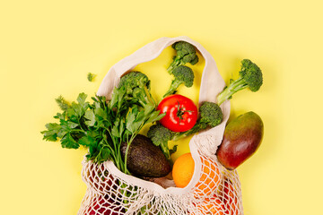 Mesh shopping bag with organic food on yellow paper background. Flat lay,
