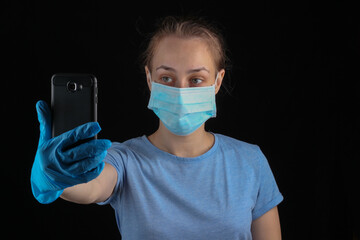 Woman in medical gloves and face mask makes selfie on the phone.