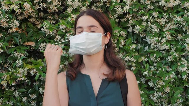 Quarantine is over concept. Young smiling woman taking off medical protective mask standing outdoors in city, office buildings. End of quarantine, covid-19 pandemic, self-isolation concept.