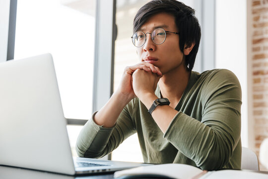 Image Of Handsome Young Asian Man Using Laptop In Apartment