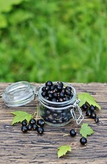 Black currant in a glass jar on a wooden table, against a background of nature. Eco-friendly...