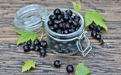 Black currant in a glass jar on a wooden table, against a background of nature. Eco-friendly product. Organic. Favorite French 