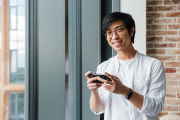 Fototapeta na wymiar Image of handsome young asian man holding cellphone in office