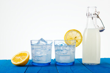 Glasses and bottle of refreshing lemonade on a blue rustic table with a white background. Summer time. Space for text.