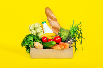 Box with different food ingredients such as fruits, vegetables, milk, yogurt, eggs on yellow background