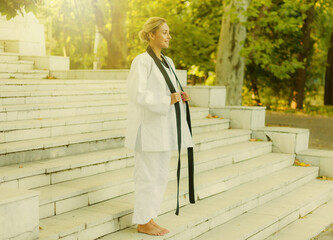 Portrait of a cheerful fighter woman in white kimonos with black belt outdoors
