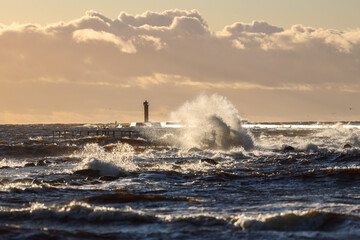 Fototapeta na wymiar Late sunset view of old lighthouse pier and large storm waves.