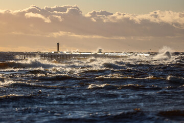 Late sunset view of old lighthouse pier and large storm waves.