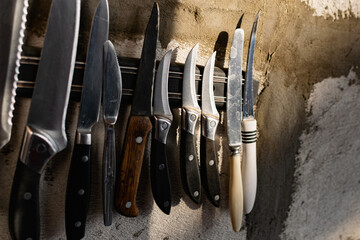 A set of metal knives of different sizes and shapes, hanging on a horizontal magnet holder. On a...