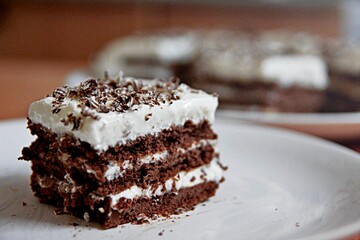 Slice of chocolate cake white cream on plate. Chocolate cake with whipped cream made for mothers day on table close up. Sweet chocolate brownie cake on background of pieces for cafe or bakery menu