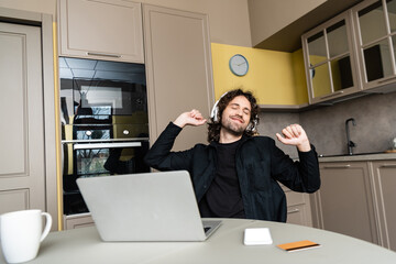 Selective focus of smiling freelancer listening music in headphones near credit card, gadgets and cup on kitchen table