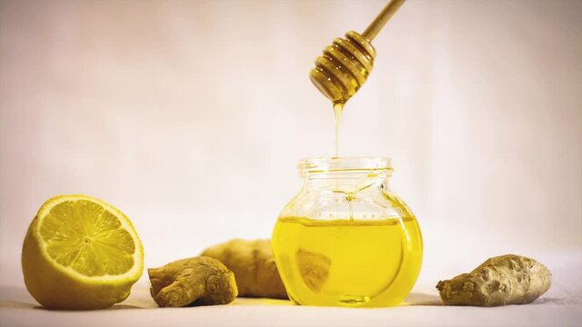 dipping wooden stick for honey in liquid honey in a glass jar, cold medicine with lemon ginger and honey, white background