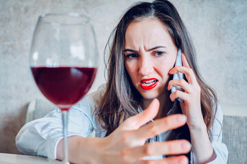 Angry girl talking on a smartphone with a glass of wine.