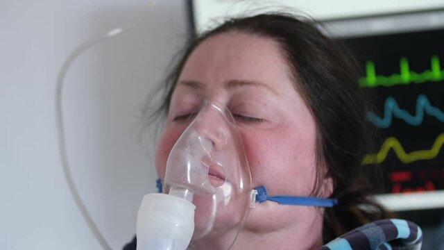sick woman with her eyes closed with an inhaler mask in the background of a monitor with vital indicators