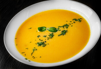 Pumpkin soup in white plate on black wooden table background