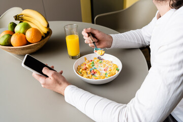 cropped view of man holding smartphone with blank screen while having breakfast