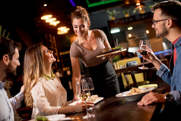 Waiter woman serving group of friends with food in the restaurant