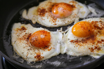 Fried eggs im black pan, macro, seasoned with paprika powder