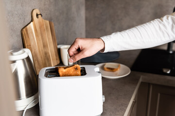 Fototapeta na wymiar partial view of man taking bread out of toaster in kitchen