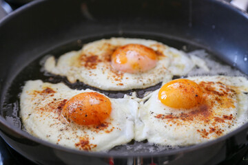 Fried eggs im black pan, macro, seasoned with paprika powder