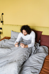 Fototapeta premium KYIV, UKRAINE - APRIL 25, 2020: high angle view of concentrated young man playing video game in bed