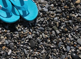 Blue flip-flops are standing on the wet pebbles on the beach.
