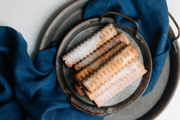 Wafer rolls on a black metal tray, blue linen napkin, selective focus