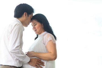 Happy Asian man hugging his pregnant wife standing at home. Love happy family concept. Pregnancy and parenthood concept.