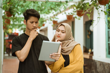 students male and hijab girl worries when looking to the screen of the tablet about wrong assignment