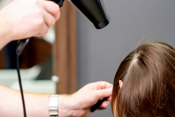 Fototapeta premium Hairdresser's hands blow drying hair of woman at the beauty salon.